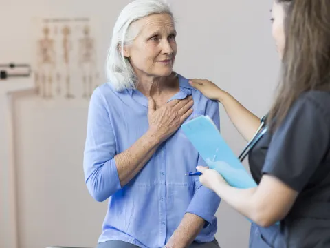 A senior woman clutching her chest, with a tech taking her blood pressure.