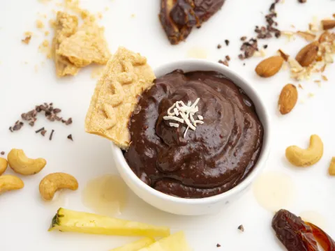 Carob pudding in bowl with a pie crust garnish, surrounded by decorative nuts