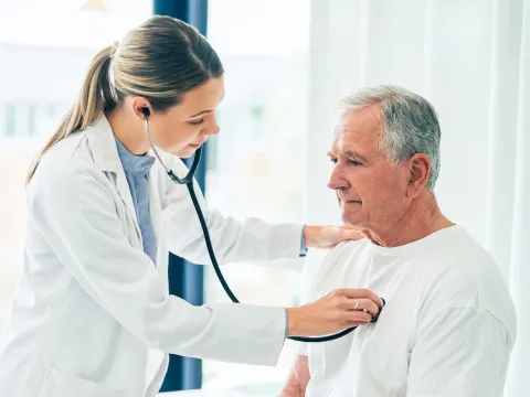Doctor checking an older male patient's lungs with a stethoscope.