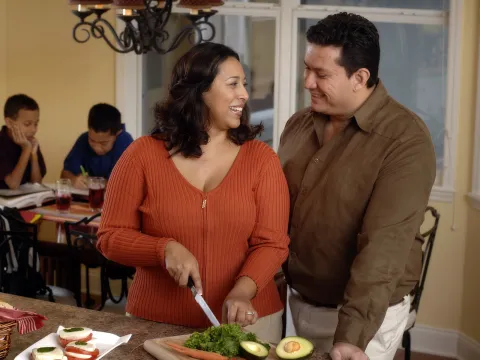 A Hispanic couple prepares a healthy meal for their family in the kitchen.