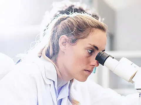 A female lab technician looking through a microscope.