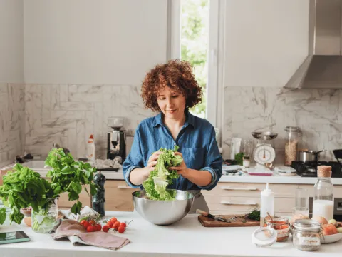 A woman making a bowl of salad in the kitchen.