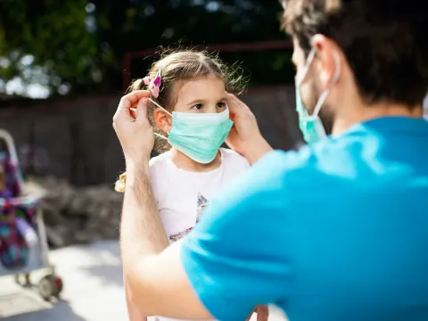 A father putting a mask on his daughter before going out
