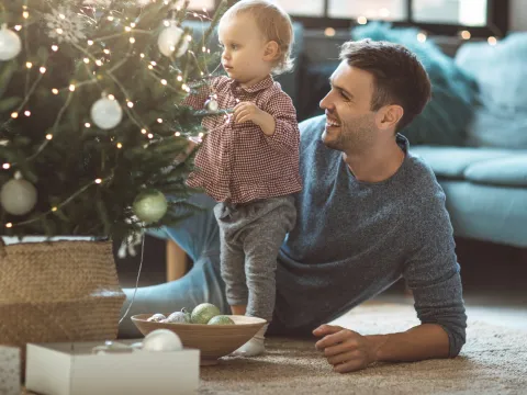 A father and his toddler trim a Christmas tree.