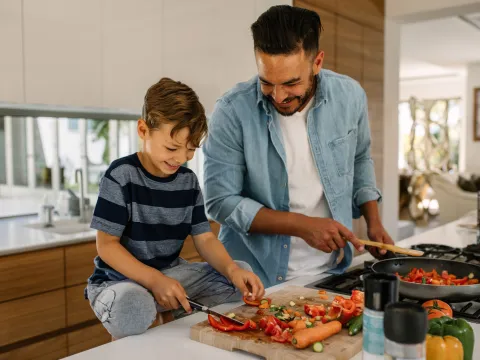 A father an son laugh together while preparing a healthy meal.
