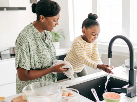 A mother and daughter wash their hands in the kitchen.
