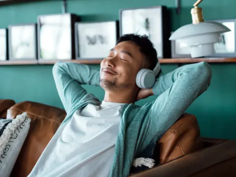 A man relaxing on a couch at home while wearing headphones.