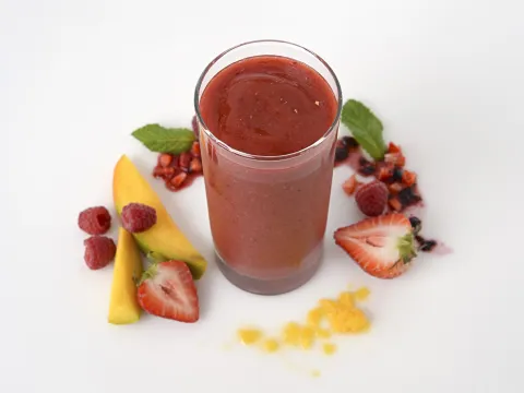 a tall glass of smoothie, surrounded by chopped mango and mixed berries
