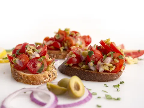 three pieces of bruschetta-topped toast with olive garnish