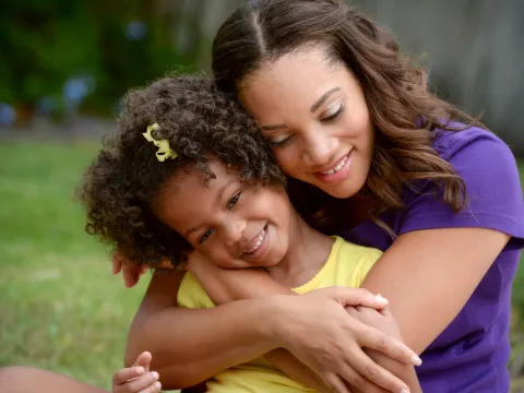 A mother hugs her daughter from behind.