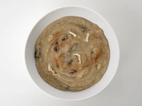 a bowl of hot cooked breakfast cereal mixed with raisins and shredded coconut