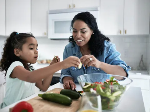 A mother and daughter prepare a salad at home.