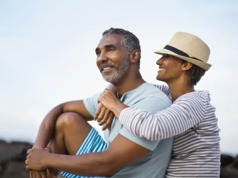 A smiling woman wraps her arms around her husband outdoors