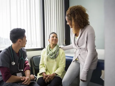 A woman sitting in a waiting room is comforted by a friend while an Adventist Health physician sits by her side