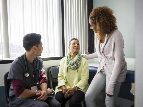 An African American daughter consoles her mother upon hearing medical news from the nurse.