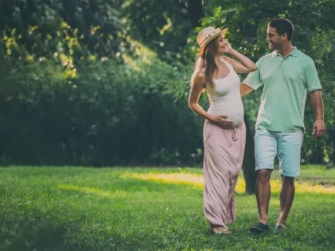 A pregnant woman walking outdoors with her husband.