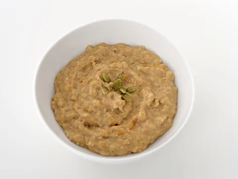 a bowl of hot breakfast cereal, mixed with pumpkin puree and topped with a sprinkle of pumpkin seeds