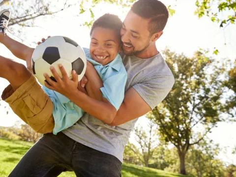 Father and son playing soccer in the park.
