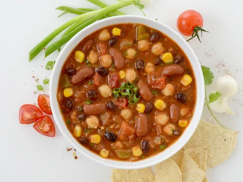Bowl of three bean chili with corn and tomato and chive garnishes