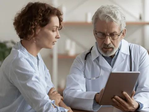 A middle-aged woman and her doctor look at a tablet.