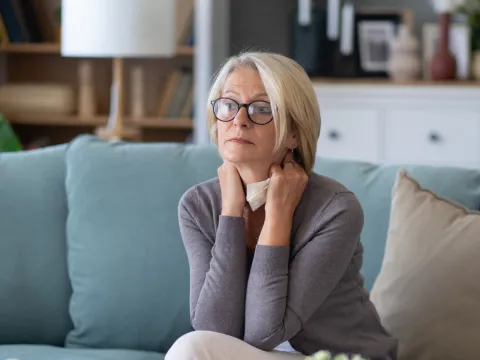 Woman sitting on a couch at home while holding a tissue.