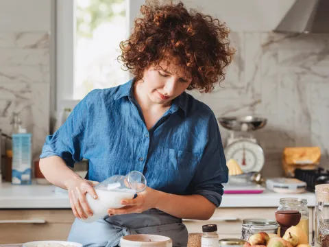 Woman pouring milk into a bowl while in a kitchen at home.