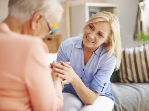 A middle-aged woman and her elderly mother hold hands.