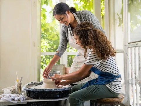 An elderly woman teaching a friend how to sculpt a bit of clay.