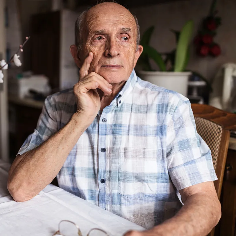 A Man Looks Seriously Out a Window of His Home