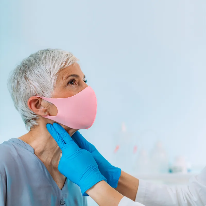A Doctor examines a patient's neck while they both wear face coverings