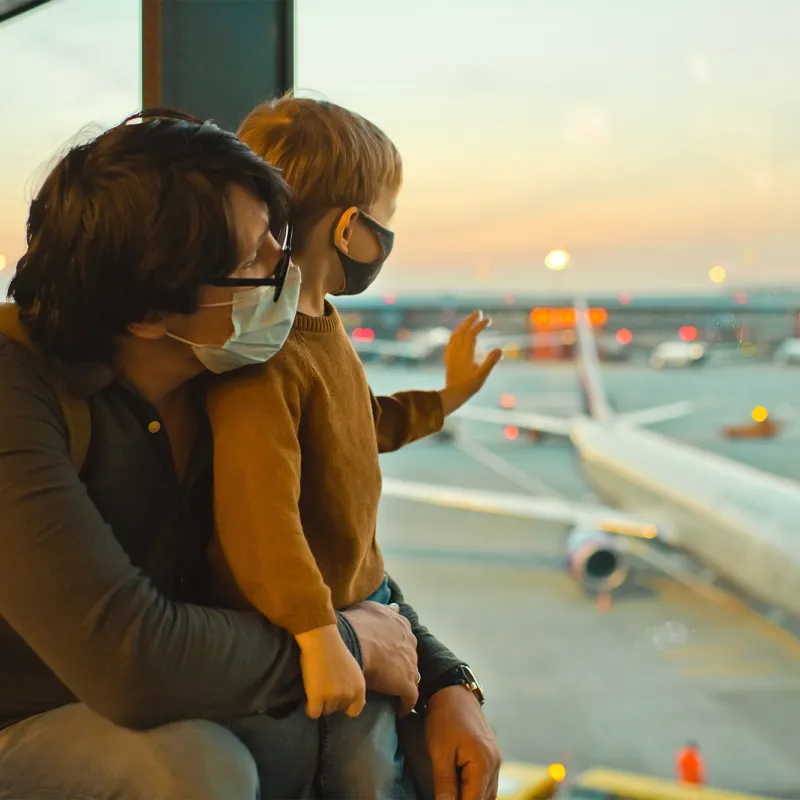 Father and son watch planes at the airport before boarding wearing face masks