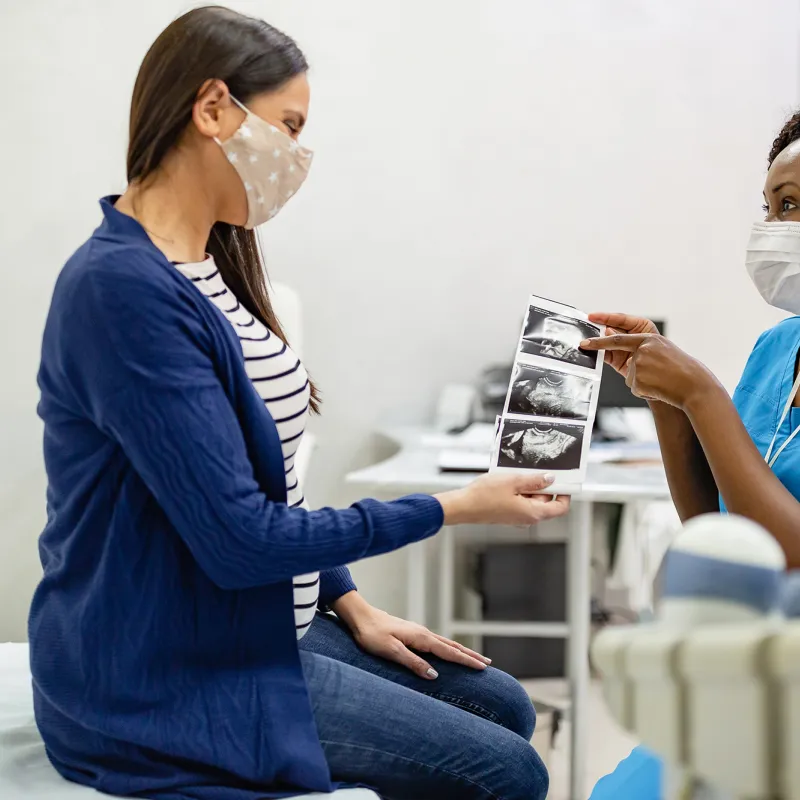 A Woman Looks Over The Sonogram of Her Baby with Her Physician.