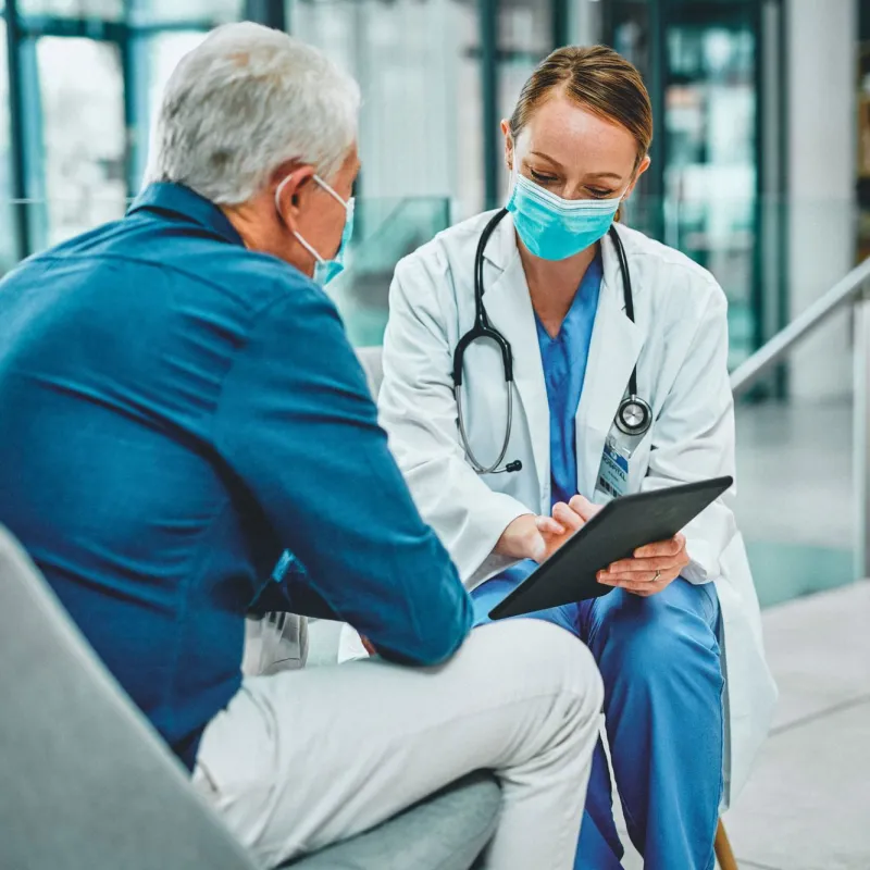 A female physician talking to a grey-haired gentleman with her tablet
