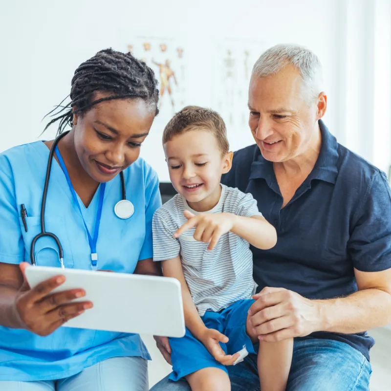 A Doctor Reviews a Patient's Chart with a Pediatric Patient and His Father in an Exam Room.
