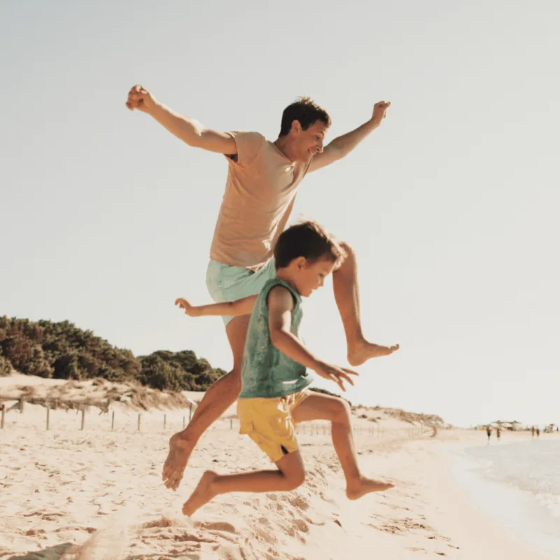A Father and Son Jump Off a Dune on the Beach