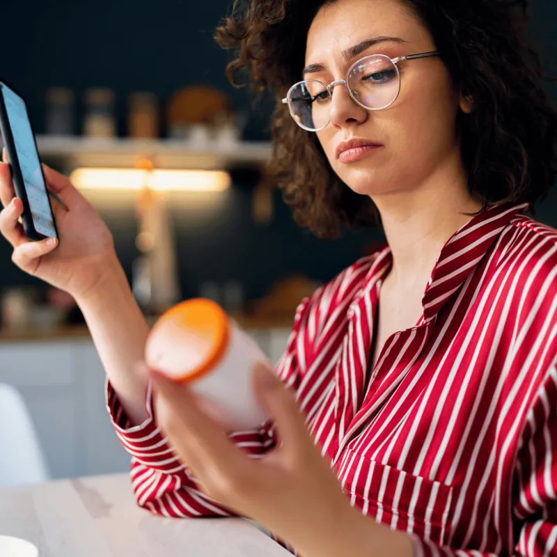 A Woman Looks at a Bottle While Researching it on Her Phone.