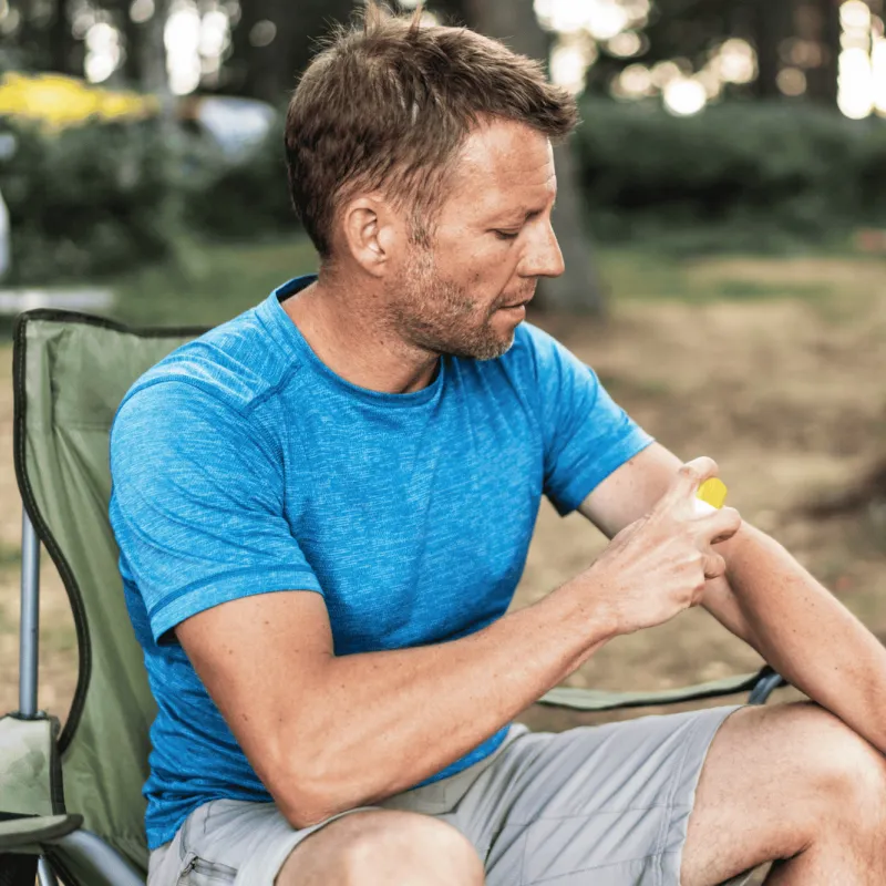A Man Scratches His Arm While Camping in a Park