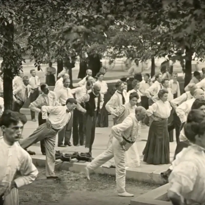 Old photograph of people balancing on one leg and stretching outdoors.