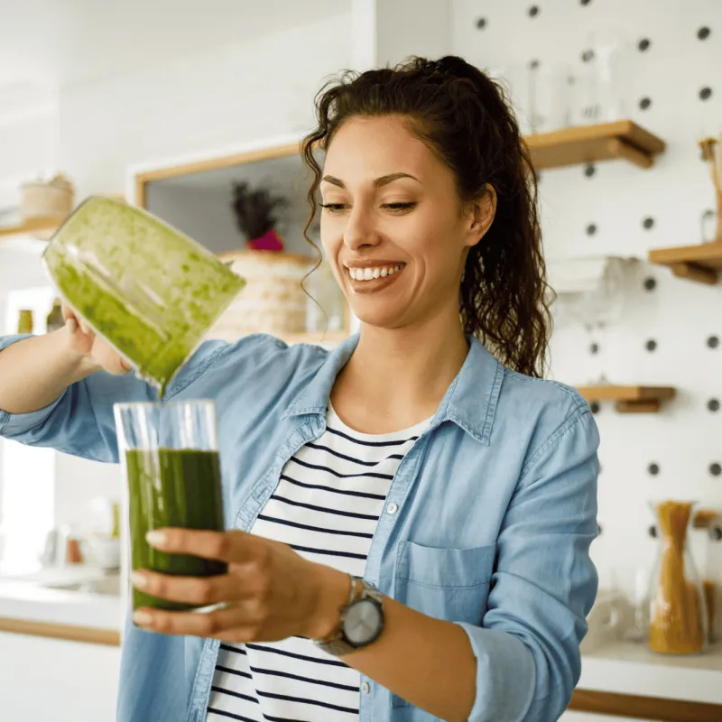 A woman pouring a green smoothie into a cup.