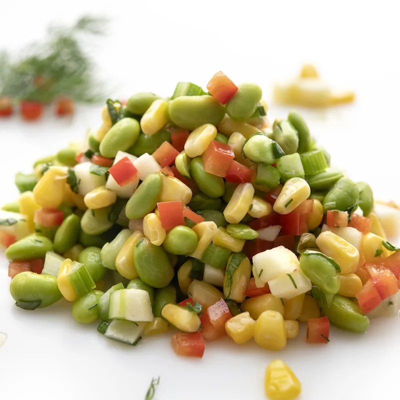Mound of edamame corn salad on white surface