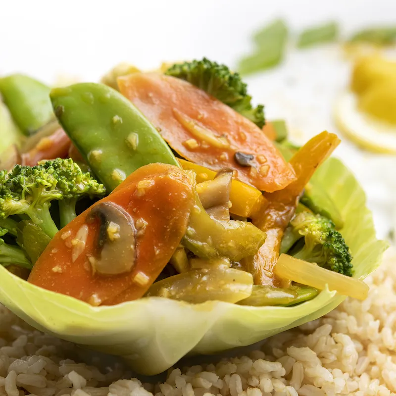 Lettuce bowl filled with veggie stir-fry sitting on brown rice