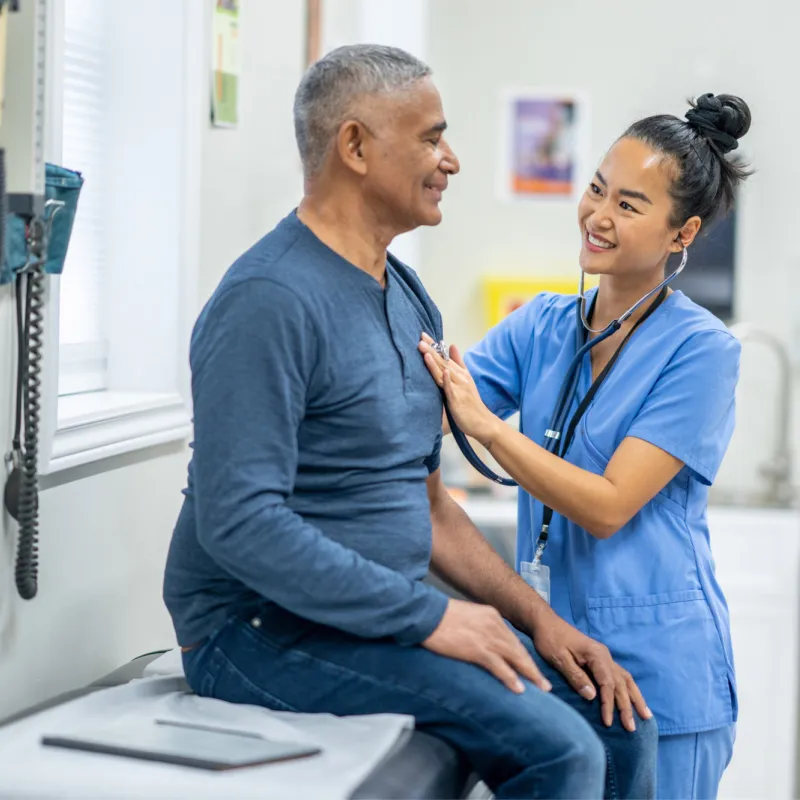 An older Hispanic man gets examined by a nurse.