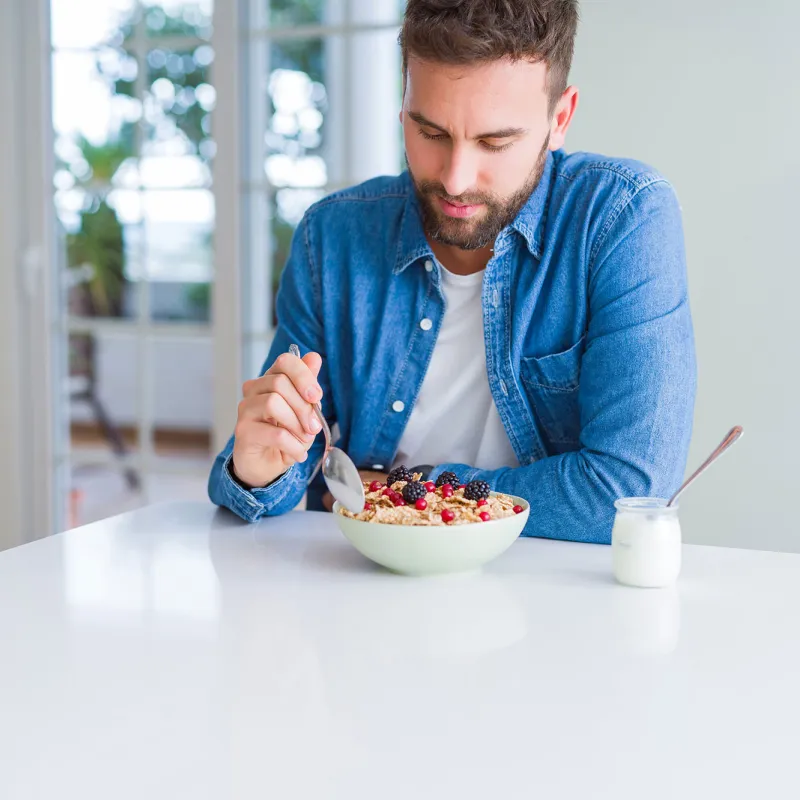 A gentleman eating a bowl of cereal with berries and a cup of yogurt