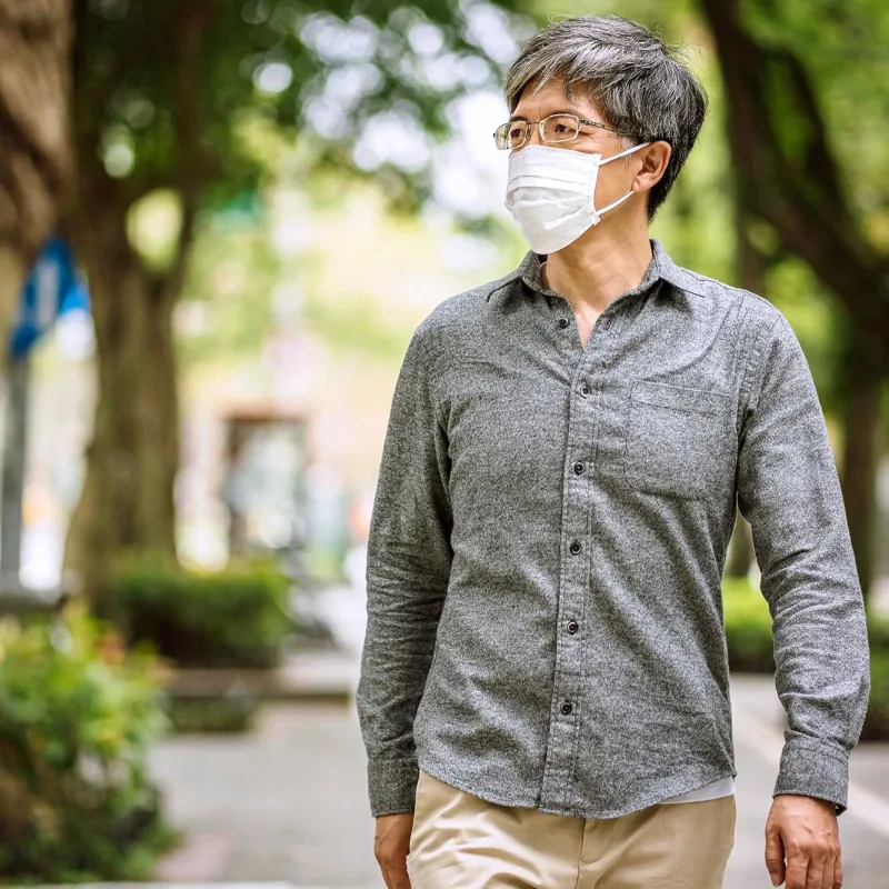 A man wearing a mask while walking outside. 