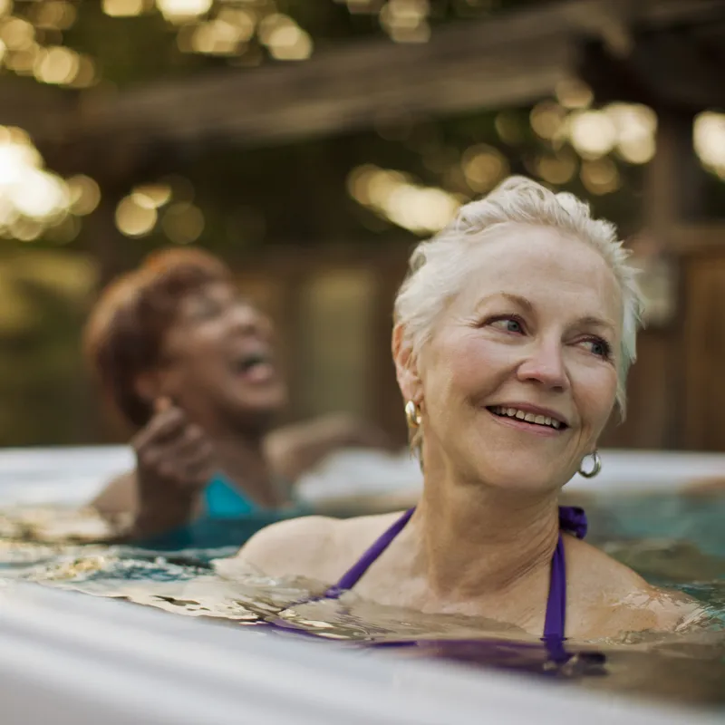 Two women laugh while soaking in an outdoor spa