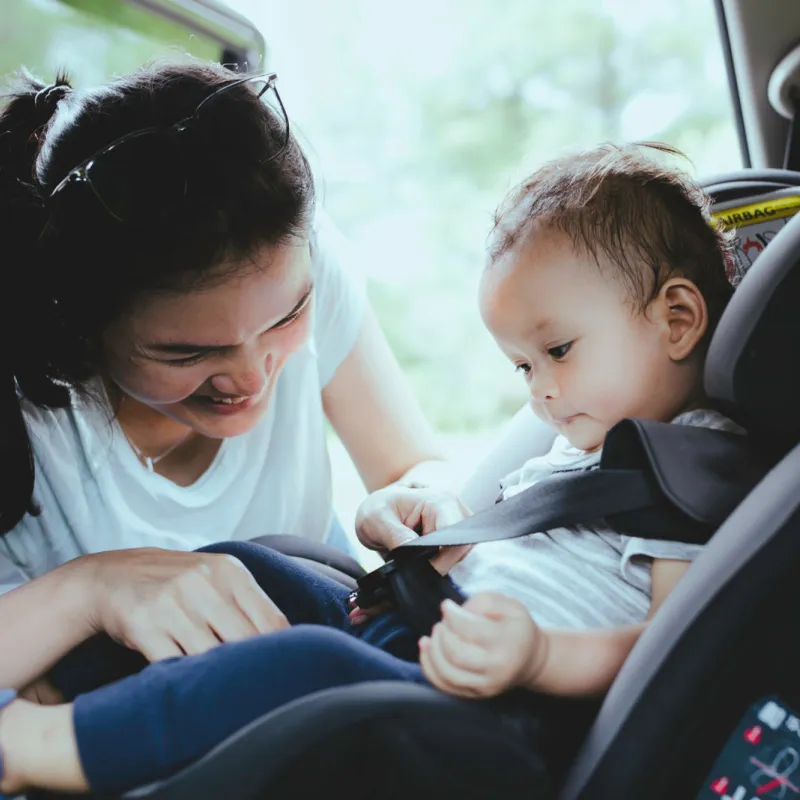 A mother buckles her child into a car seat in the back of a car.