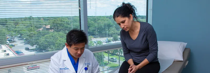 Iswanto Sucandy showing patient a something on a laptop while she's sitting on examination table.