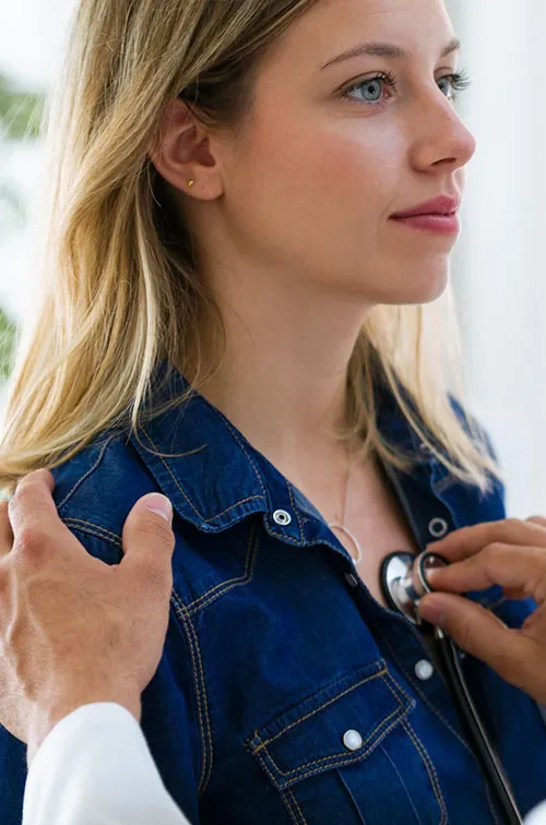 Doctor listening to woman's heart, a hand on her shoulder and a stethoscope 