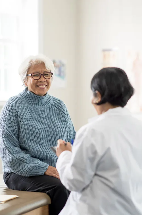 An older female patient talking to a female physician in an exam room.