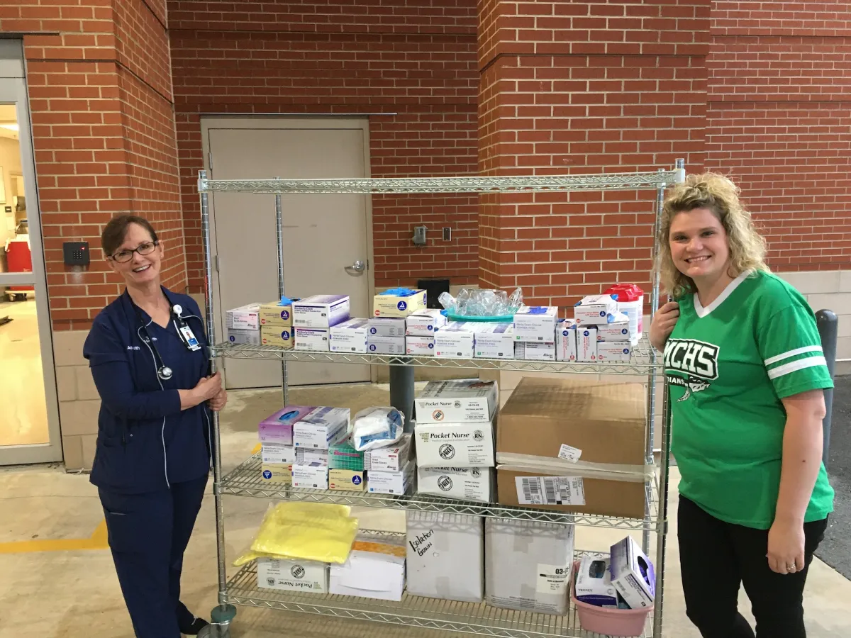 Two women standing next to a shelf filled with donations.